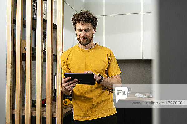 Gut aussehender Mann  der ein digitales Tablet benutzt  während er in der heimischen Küche steht