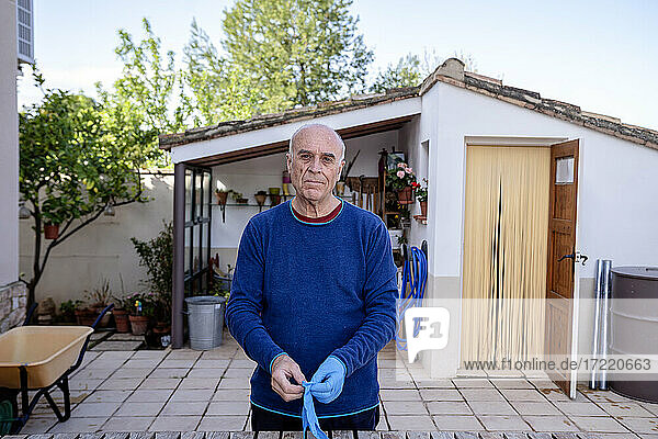 Älterer Mann trägt Handschuh  während er im Hinterhof steht