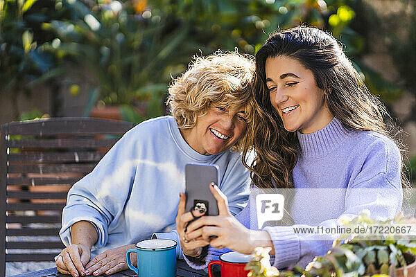 Smiling young woman taking selfie with mature female through mobile phone at back yard