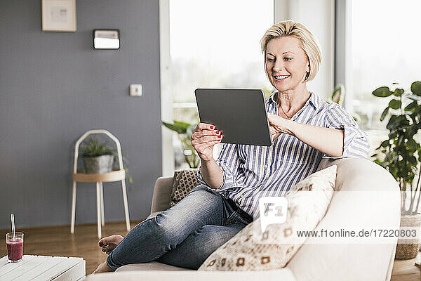Glückliche Frau  die ein digitales Tablet benutzt  während sie zu Hause auf dem Sofa sitzt