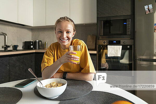 Young woman with juice sitting by table in kitchen