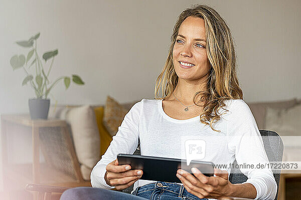 Smiling woman holding digital tablet on chair at home