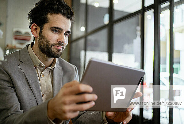 Mittlerer erwachsener Geschäftsmann  der in einem Café an einem digitalen Tablet arbeitet