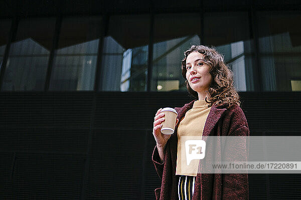Schöne Frau beim Kaffee trinken vor einem Glasgebäude stehend
