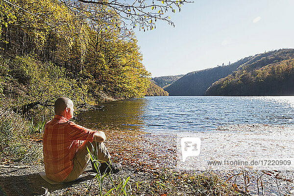 Senior man relaxing on shore of Rursee reservoir in autumn