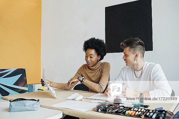 Junges multiethnisches Paar  das im Atelier sitzend über Kalligrafie-Schrift diskutiert