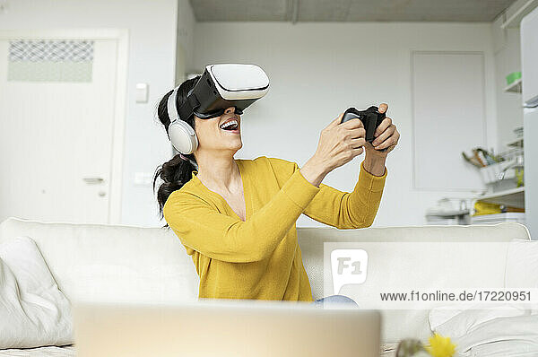 Lachende Frau  die mit einem Virtual-Reality-Headset zu Hause ein Spiel spielt