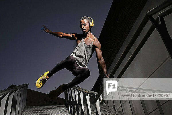 Young African man with headphones jumping at staircase