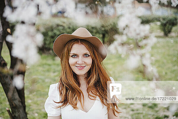 Lächelnde rothaarige Frau mit Hut  die im Park steht