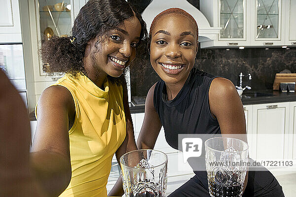 Porträt von zwei glücklichen Freunden  die in der Küche ein Selfie mit dem Smartphone machen