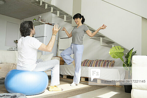 Frau unterrichtet Mann  der auf einem Fitnessball sitzt  im Wohnzimmer zu Hause in Yoga