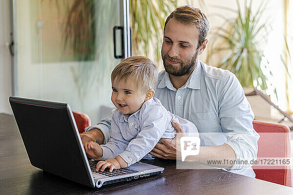 Lächelnder süßer Junge  der einen Laptop vor seinem Vater am Tisch benutzt