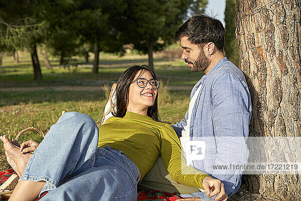 Lächelnde Frau im Gespräch mit ihrem Freund  während sie sich beim Picknick im Park entspannt