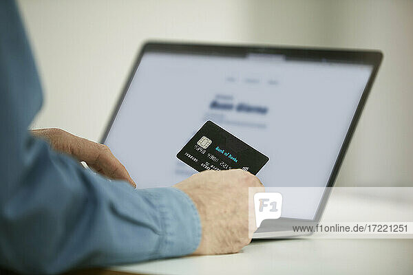 Mann beim Bezahlen mit Kreditkarte beim Online-Shopping am Laptop im Büro