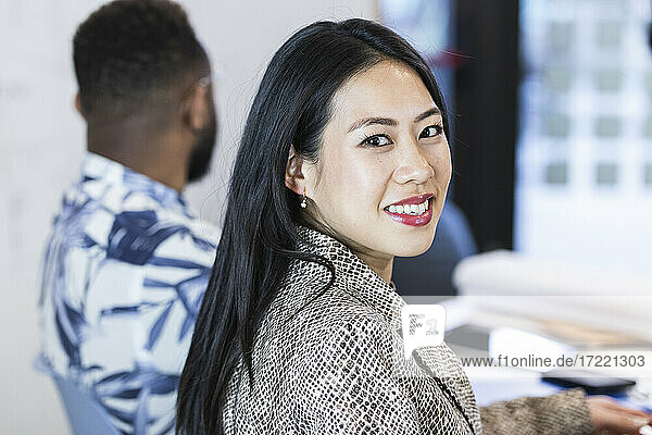 Smiling businesswoman with colleague in background at office