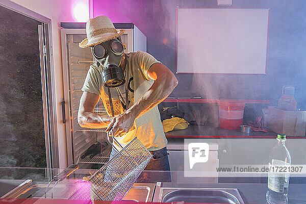 Mature man in gas mask preparing food in deep fryer at commercial kitchen