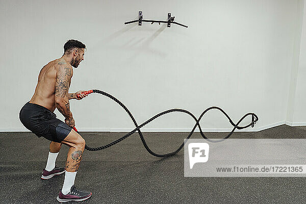 Mid adult male athlete exercising with rope while standing at health club