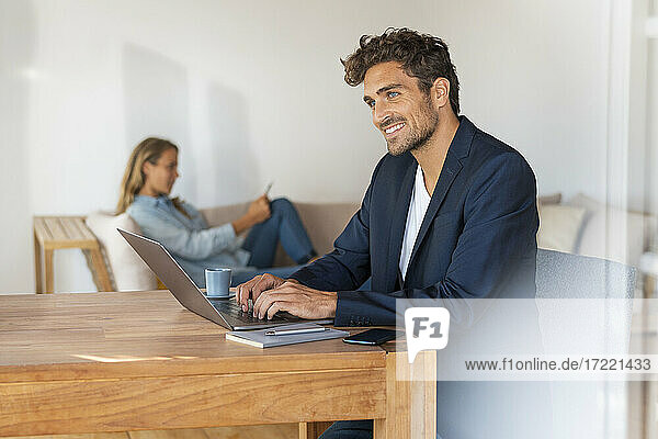 Nachdenklicher Mann mit Laptop auf dem Tisch  während seine Freundin zu Hause im Büro sitzt