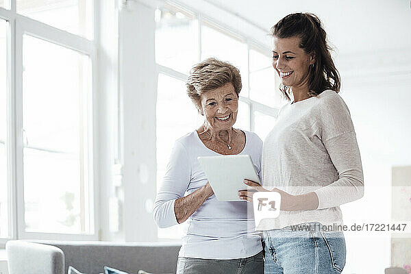 Lächelnde Großmutter und junge Frau schauen auf ein digitales Tablet