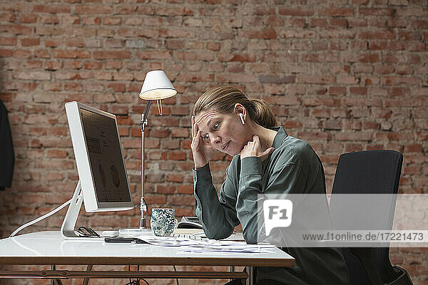 Overworked businesswoman with head in hands sitting at desk in office
