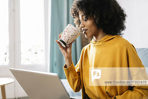 Frau trinkt Kaffee  während sie zu Hause am Laptop sitzt
