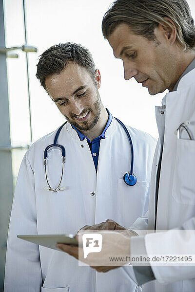 Männlicher Arzt im mittleren Erwachsenenalter  der mit einem Kollegen über ein digitales Tablet im Krankenhaus die Behandlung bespricht