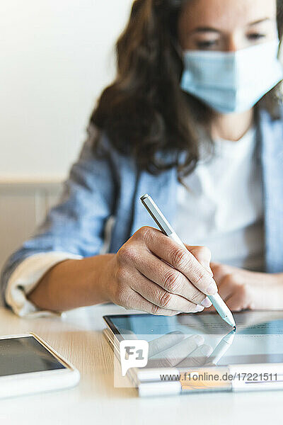 Geschäftsfrau mit digitalisiertem Stift bei der Arbeit auf einem digitalen Tablet in einem Café Pandemie
