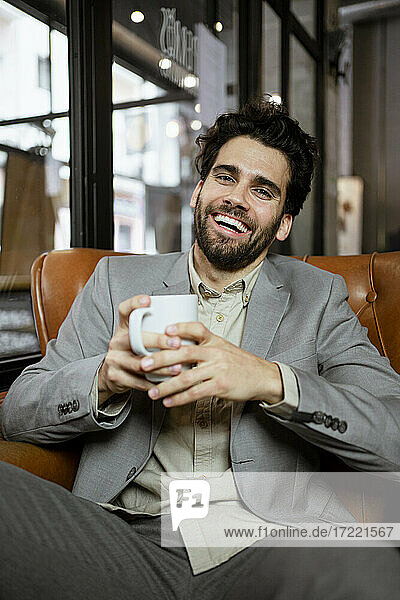 Cheerful businessman holding coffee cup while sitting in coffee shop