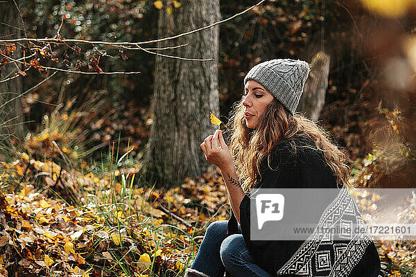 Beautiful woman with long hair blowing autumn leaf in forest during vacations