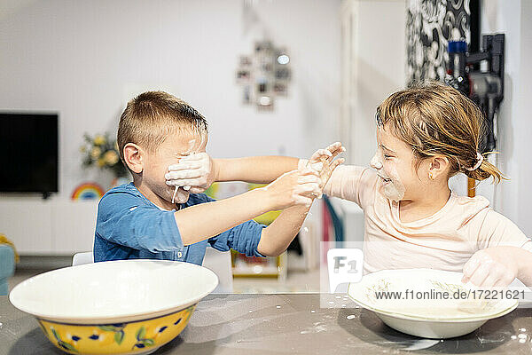 Verspielte Geschwister  die zu Hause Gesichter mit Mehl und Wasser beschmieren