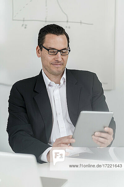 Männlicher Unternehmer  der am Arbeitsplatz sitzt und ein digitales Tablet benutzt