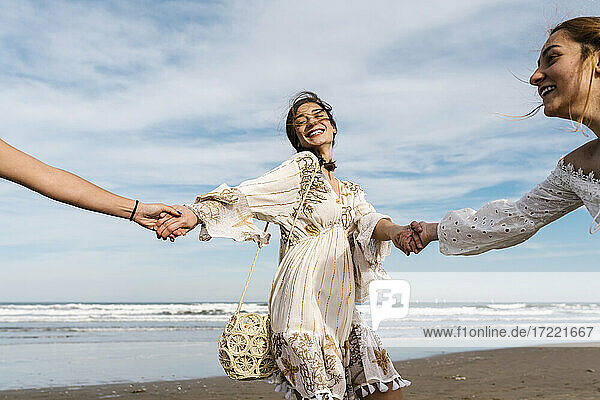 Glückliche Frau hält Hände von Freunden am Strand