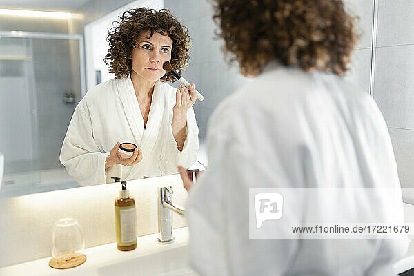 Schöne Frau trägt im Badezimmer Puder mit einem Make-up-Pinsel auf