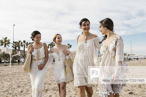 Young friends in white dresses smiling while walking at beach