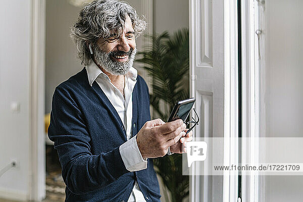Lächelnder gut aussehender Mann  der zu Hause ein Smartphone benutzt