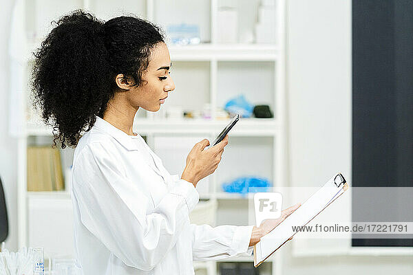 Young female researcher photographing paper on clipboard in laboratory