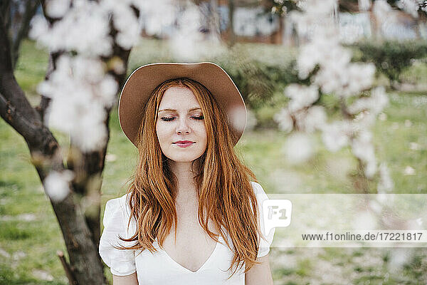 Redhead woman with eyes closed wearing hat at park