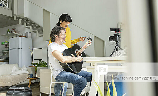 Fröhliches Paar spielt Gitarre beim Vlogging zu Hause