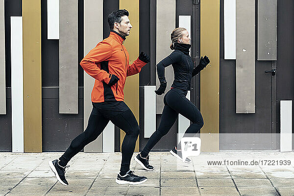 Entschlossene männliche und weibliche Freunde joggen auf dem Fußweg an der Mauer