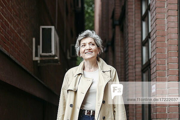 Smiling mature woman looking away while standing by building