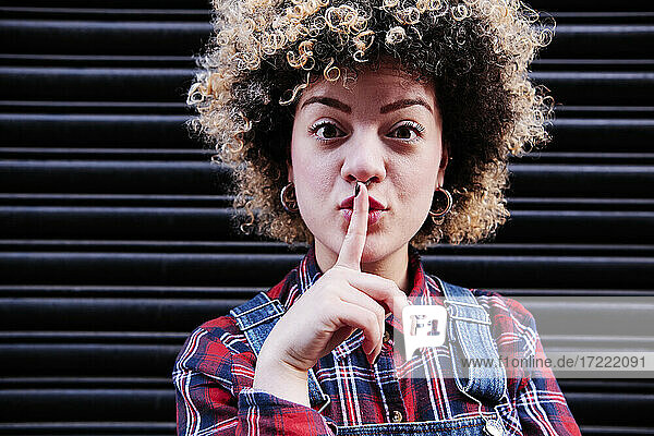 Young curly haired woman with finger on lips in front of shutter