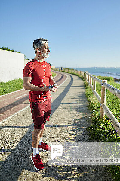 Mann hält Smartphone  während er an einem sonnigen Tag auf dem Fußweg steht