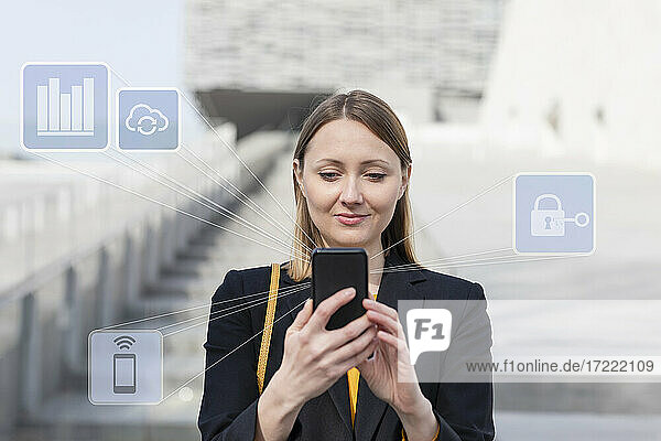 Businesswoman using mobile phone while standing with networking icon outdoors