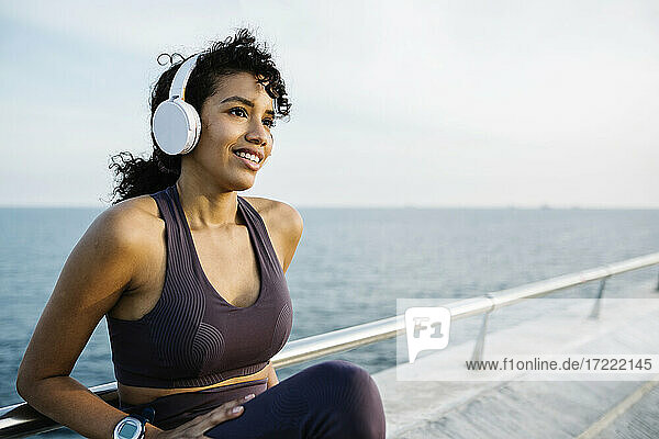 Nachdenkliche Sportlerin mit Kopfhörern auf einer Brücke sitzend