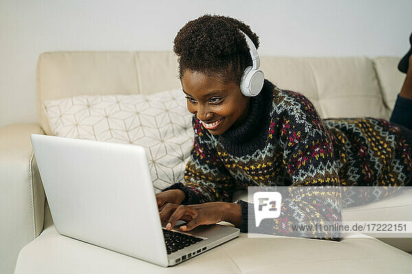 Smiling female entrepreneur with headphones working on laptop in living room