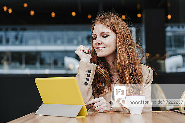 Rothaarige Frau schaut in einem Café auf eine digitale Tafel