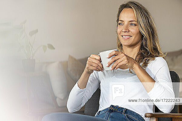 Smiling woman looking away while having coffee at home