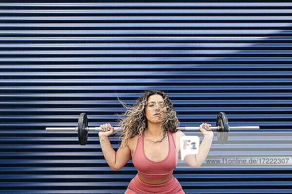 Sportswoman exercising with barbell in front of blue wall