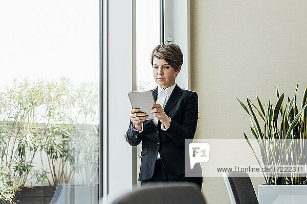 Unternehmerin  die ein digitales Tablet benutzt  während sie im Büro am Fenster steht