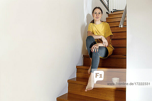 Lächelnde Frau auf der Treppe zu Hause sitzend